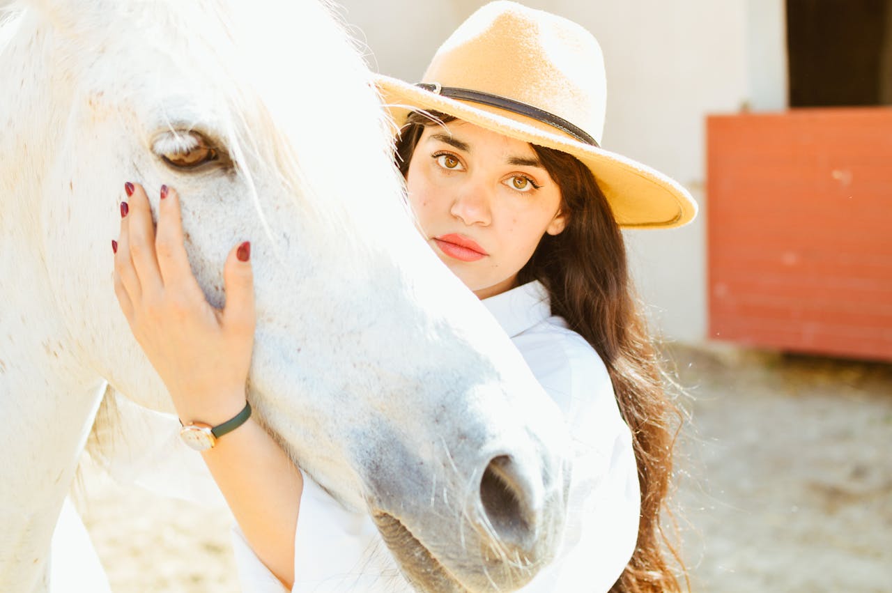 Woman in a hat lovingly caresses a white horse outdoors, creating a warm and serene moment.